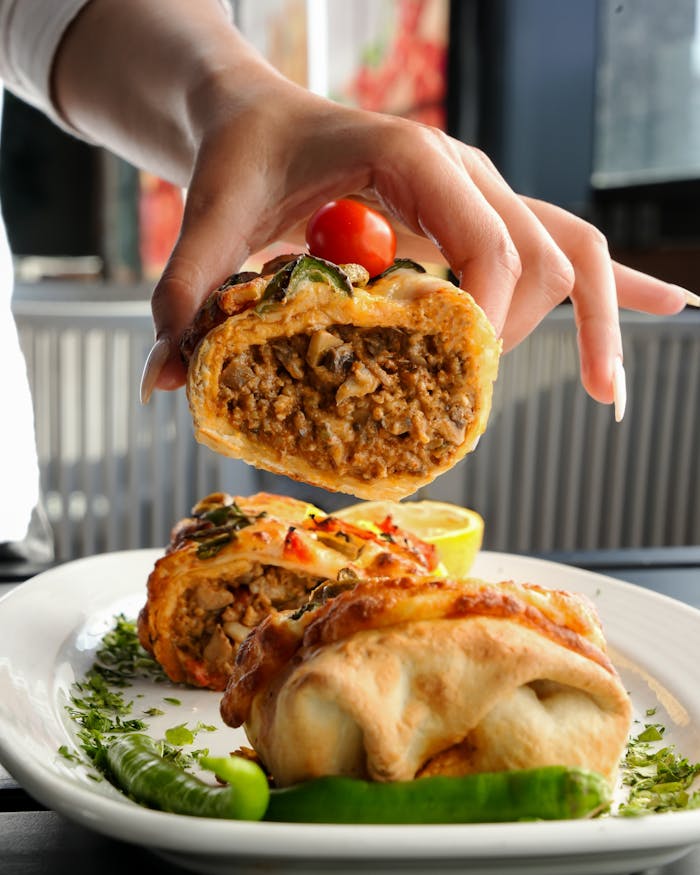 pexels-photo-28732301 Hand holding a savory stuffed bread roll with meat filling in a restaurant setting.